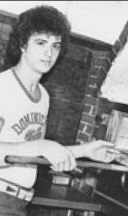 A young man holding a baseball bat in front of a brick wall.